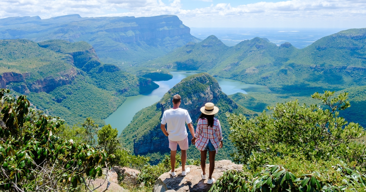 Doi turiști admirând priveliștea spectaculoasă asupra unui canion verde și a unui râu sinuos din Africa de Sud, aproape de Cascada Victoria.