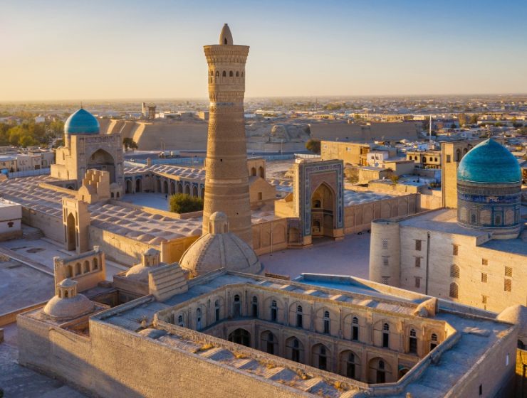 Panoramă asupra unui oraș istoric din Uzbekistan, cu moschei și clădiri tradiționale iluminate de lumina apusului.